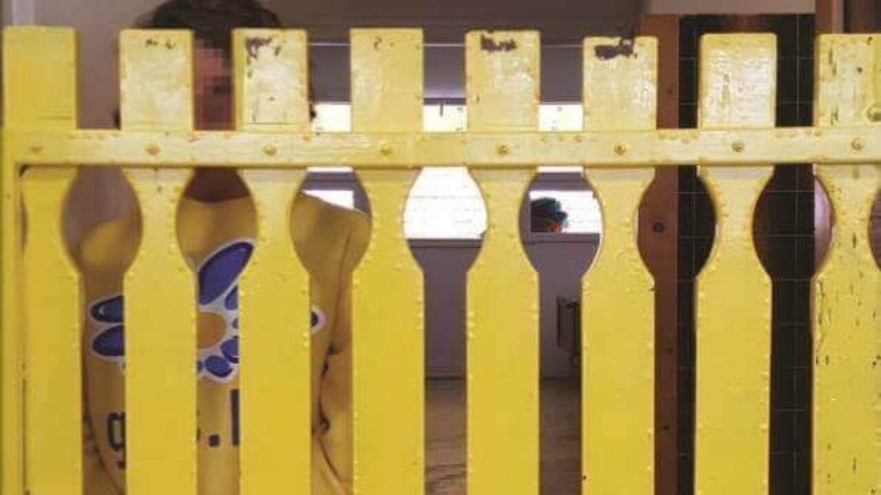 Image of a young person standing behind a tall wooden gate in an institution