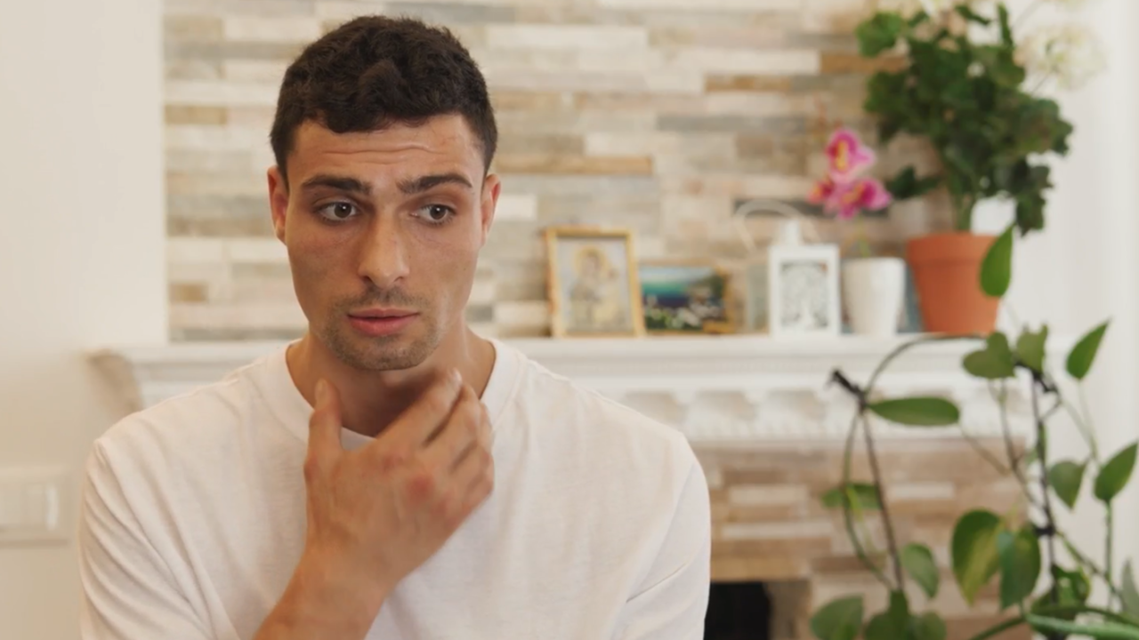 Closeup photo of Victor. He has short dark hair, brown eyes, and he is gesticulating with his hand towards his throat as he speaks. He looks a bit nervous.